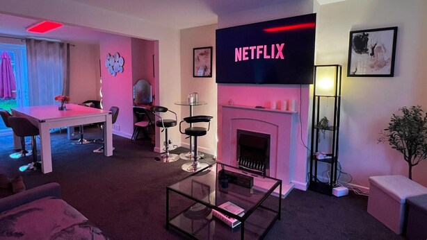 A modern living room with a fireplace, a flat-screen TV displaying 'NETFLIX', and a dining area with a table and chairs.