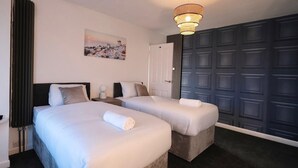 A hotel room with two beds, a painting on the wall, a dark door, and a chandelier.