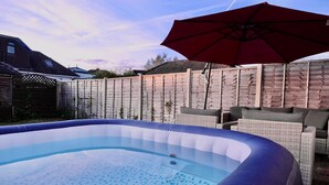 A backyard with a swimming pool, wicker furniture, and a red umbrella.