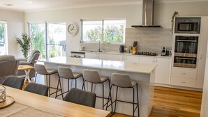 A modern kitchen with a central island, bar stools, a dining table, and built-in appliances. - Peppermint Rise - a luxurious retreat in Peppermint Grove Beach, WA. (Peppermint Grove Beach)