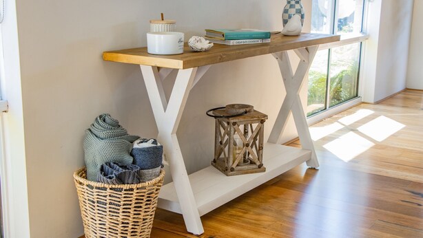 A wooden console table with a white vase, a book, and a checkered vase. A woven basket with blankets is below the table. - Peppermint Rise - a luxurious retreat in Peppermint Grove Beach, WA. (Peppermint Grove Beach)
