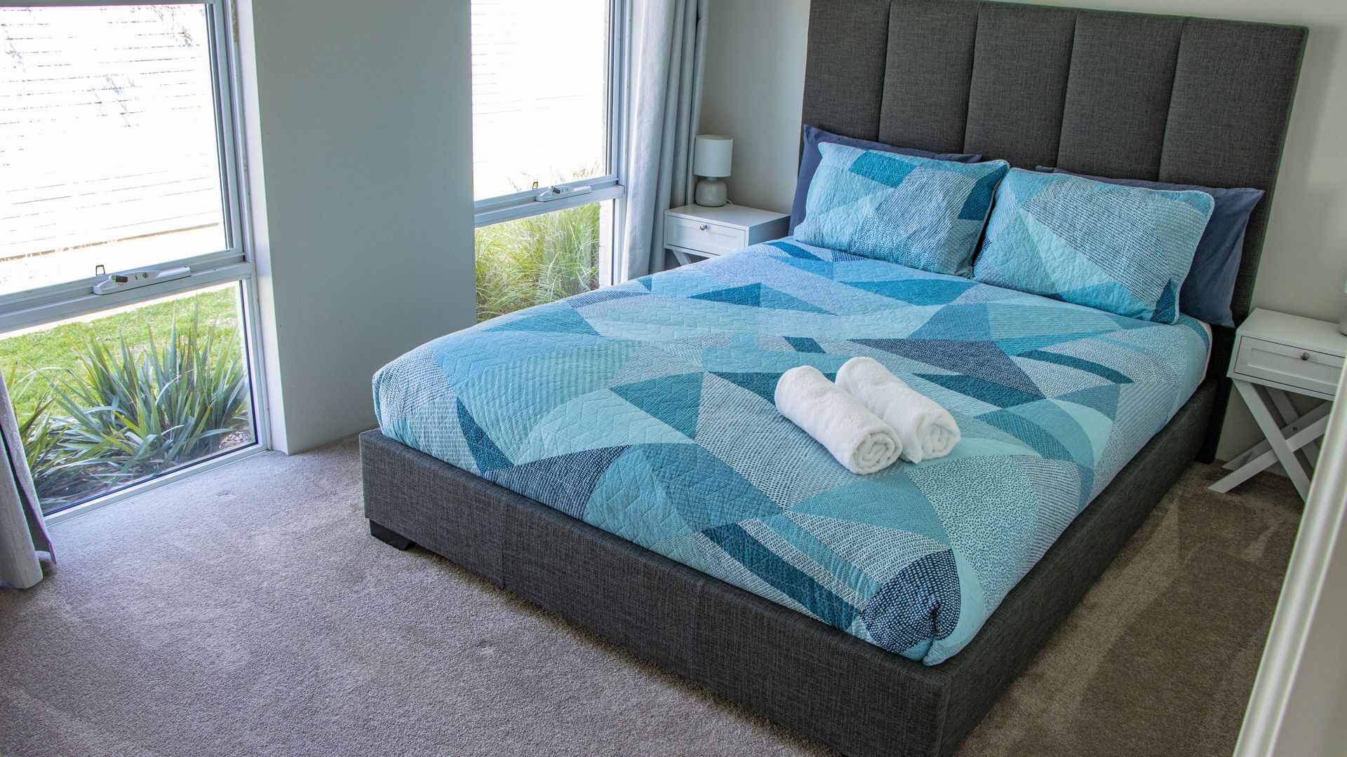 Une chambre à coucher avec un lit, une table de chevet, une fenêtre et une vue sur la verdure.