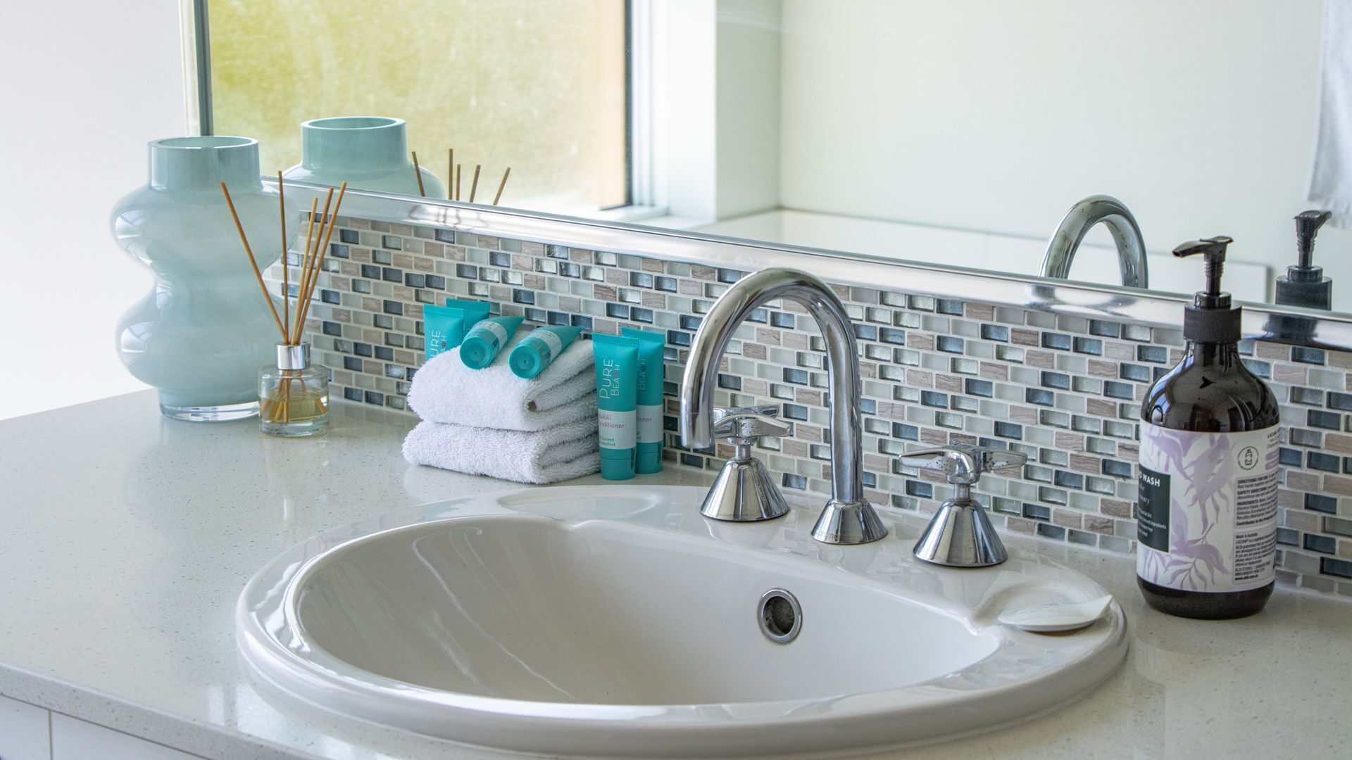 Un baño con un lavabo blanco, dos llaves, un espejo y una ventana.