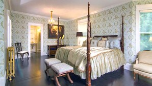 Una camera da letto con un letto a baldacchino, una panca, una toeletta con uno specchio e un lampadario.
