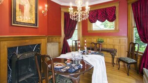 Una sala da pranzo con camino in marmo, pareti rosse e un lampadario.