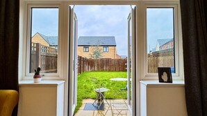 On aperçoit, à travers une porte vitrée, un jardin avec une pelouse, une table et des chaises.