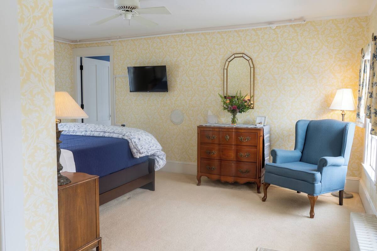 A bedroom with a bed, dresser, chair, TV, and a mirror.