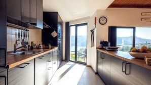 Een moderne keuken met een houten aanrecht, roestvrijstalen apparatuur en uitzicht op een bergachtig landschap door een groot raam.