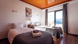 Een hotelkamer met twee bedden, een houten plafond, een groot raam met gordijnen en een schilderij aan de muur.