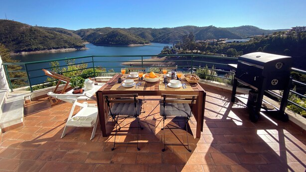 Een terras met een ontbijt tafel, met uitzicht op een meer en heuvels.