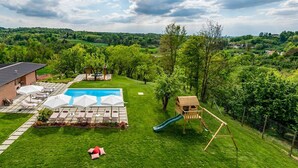 Ein Garten mit Swimmingpool, Liegestühlen, einer Rutsche und einem hölzernen Spielhäuschen.