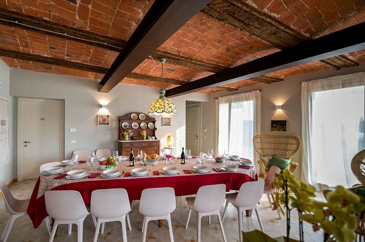 A dining area with a brick ceiling, white chairs, a table set for six, and a chandelier.