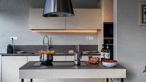 Eine moderne Küche mit einer zentralen Kochinsel, einem Edelstahl-Dunstabzug und einem eingebauten Backofen.
