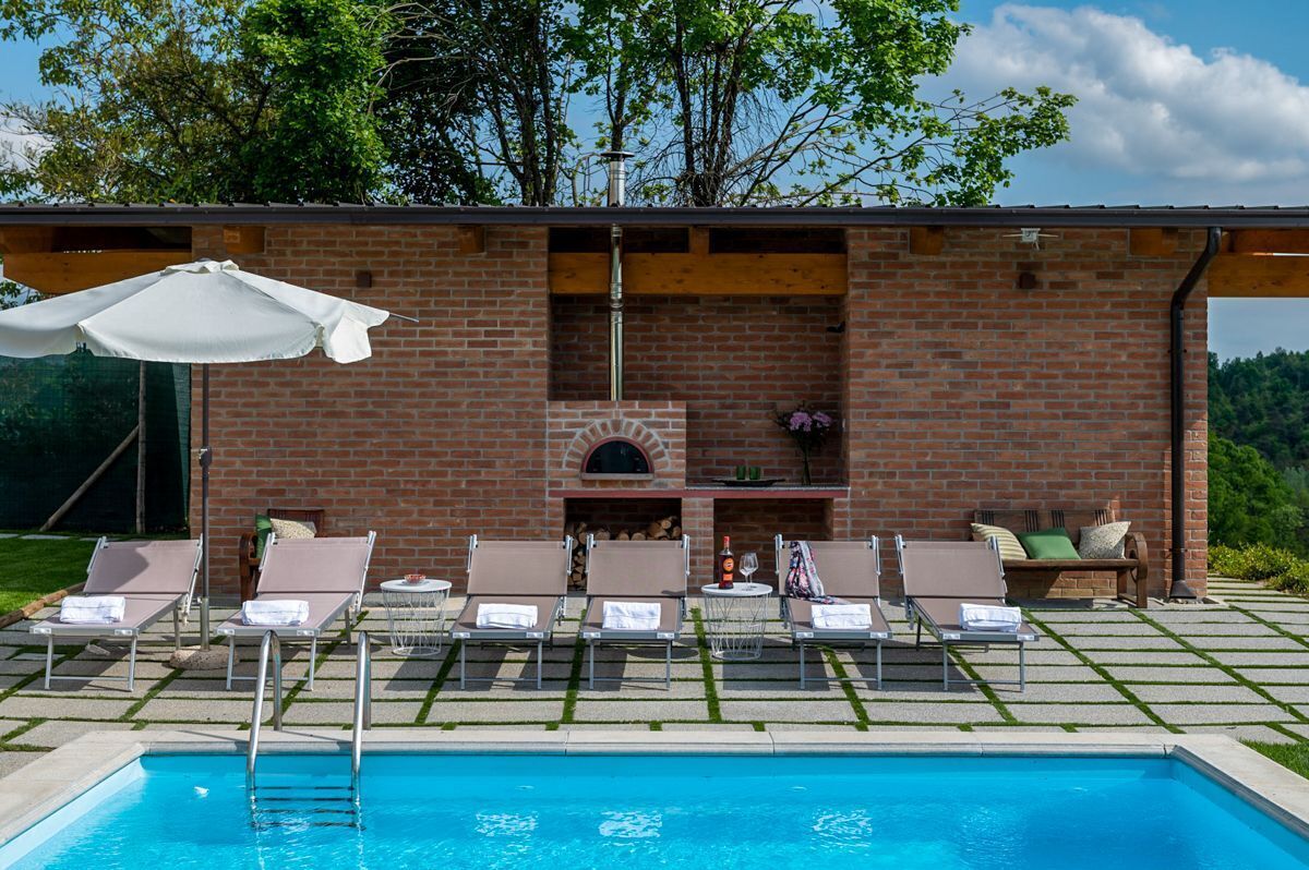 A poolside area with lounge chairs, a barbecue, and a brick wall with a chimney.