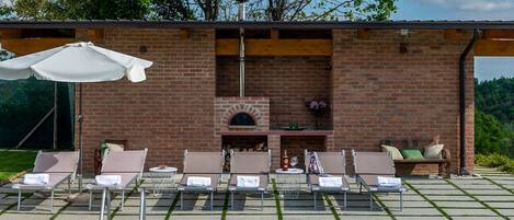 A poolside area with lounge chairs, a barbecue, and a brick wall with a chimney.