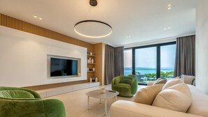 A modern living room with a flat-screen TV, green chairs, a beige sofa, and a view of the sea. - Villa Rora - Four Bedroom Villa, Sleeps 8 (Brela - Krug)