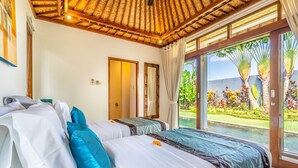 A hotel room with two beds, a large window with a view of palm trees and a pool, and a thatched ceiling.