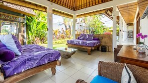 A spacious room with a bed, a sofa, and a dining area, featuring a thatched roof and large windows.