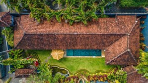 An aerial view of a villa with a tiled roof, a swimming pool, and lush tropical landscaping.