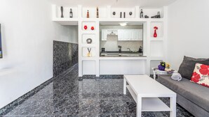 Un soggiorno moderno con pavimento in marmo, un divano bianco, un tavolino da caffè e un angolo cucina con mobili bianchi e un piano di lavoro.