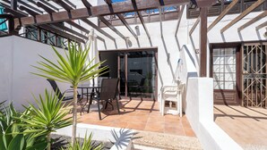 Un'area patio con una pergola, un tavolo e sedie, e una piccola sedia bianca.