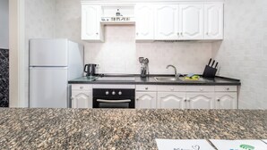 Una cucina con mobili bianchi, un piano di lavoro in granito, forno a incasso e frigorifero.