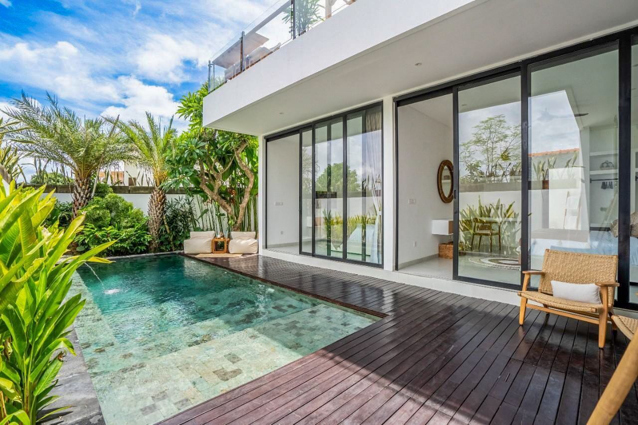 Une maison moderne dotée d’une piscine, d’une terrasse en bois et de grandes portes vitrées donnant sur un espace patio.