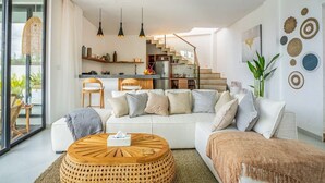 Een moderne woonkamer met een witte bank, een ronde houten salontafel en een trap naar een verdieping erboven.
