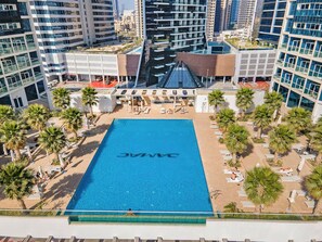 A rooftop pool with a clear blue water surface, surrounded by palm trees and lounge chairs.