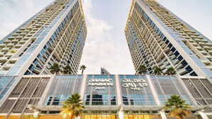 A high-rise building with two prominent towers, featuring the names "DAMAC MAISON" and "GILDAS" on the facade.