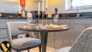 A modern kitchen with a dining area, featuring a round table set for two with wine glasses, a candle centerpiece, and a yellow napkin.