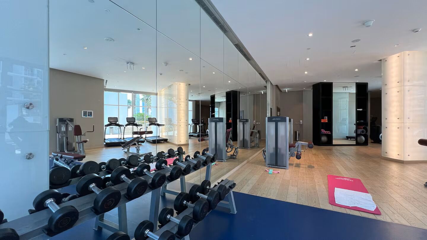 Un gimnasio con equipo de ejercicio, un muro de espejos y una colchoneta azul.