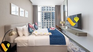 A hotel room with a bed, a TV, a desk, and a window with a view of a building.