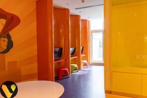 Ein lebhaft gestalteter Kinderspielbereich mit orangefarbenen und gelben Wänden, Regalen voller Spielzeug und einem weißen Tisch.