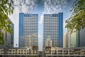 Un edificio moderno de gran altura con una fachada de ventanas y balcones, rodeado de otros edificios y zonas verdes.