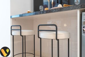 Two bar stools with cushioned seats and metal frames, a countertop with a dark backsplash, and a wall-mounted control panel.