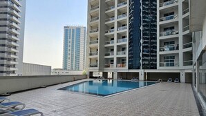 A rooftop swimming pool with lounge chairs, surrounded by high-rise buildings.