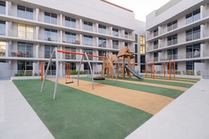 A playground with swings, slides, and a climbing structure in an outdoor area with a building in the background.