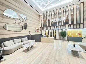 A modern lobby with a reception desk, a sofa, a coffee table, and a large mirror.