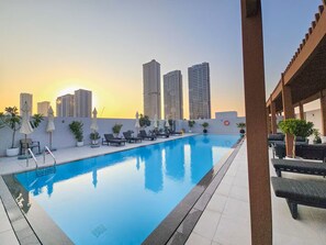 Ein Dachpool mit Liegestühlen und Sonnenschirmen, umgeben von hohen Gebäuden.