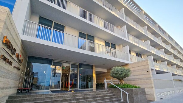 A multi-story hotel with a modern design, featuring a central entrance with glass doors, a staircase leading to the entrance, and a small tree in the foreground. - Vogue, JVC Luma22 East near Circle Mall (Dubai)