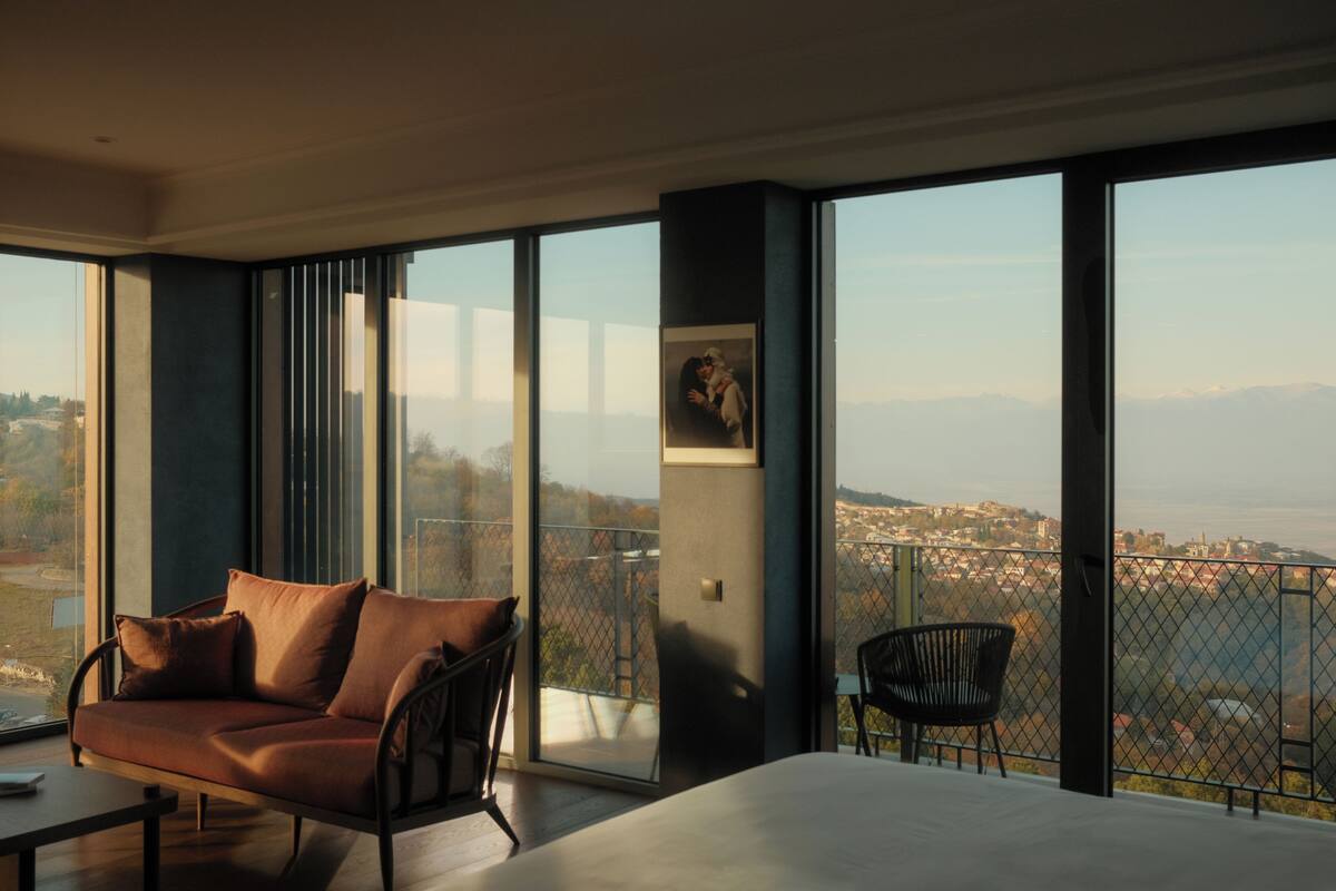 A modern hotel room with a large bed, a leather sofa, and a balcony with a city view.