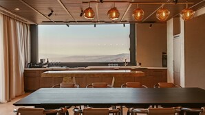 A modern kitchen with a large window, wooden cabinets, and a dining area with a long table and chairs. - BODBE Hotel (Sighnaghi)