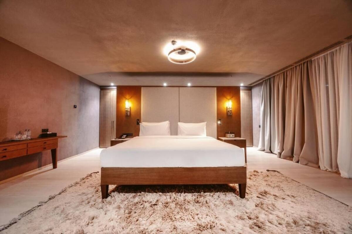 A bedroom with a large bed, wooden headboard, two bedside tables, a nightstand, a fluffy rug, and a ceiling light fixture.