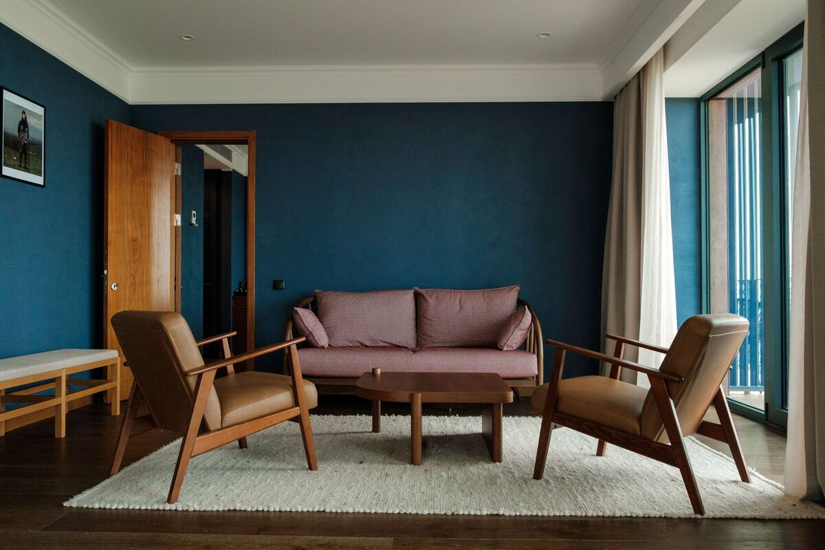 A living room with a blue wall, a wooden sofa, two armchairs, a coffee table, and a bench.