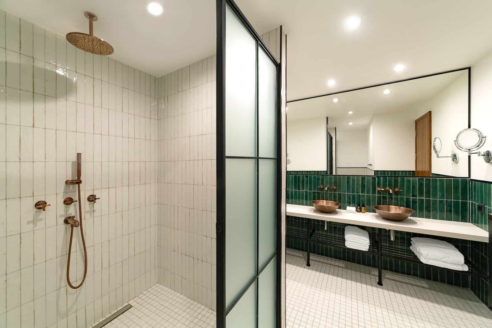 Un baño moderno con cabina de ducha de vidrio, tocador con lavabo de cobre y un espejo grande.