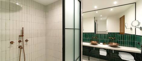 Un baño moderno con cabina de ducha de vidrio, tocador con lavabo de cobre y un espejo grande.