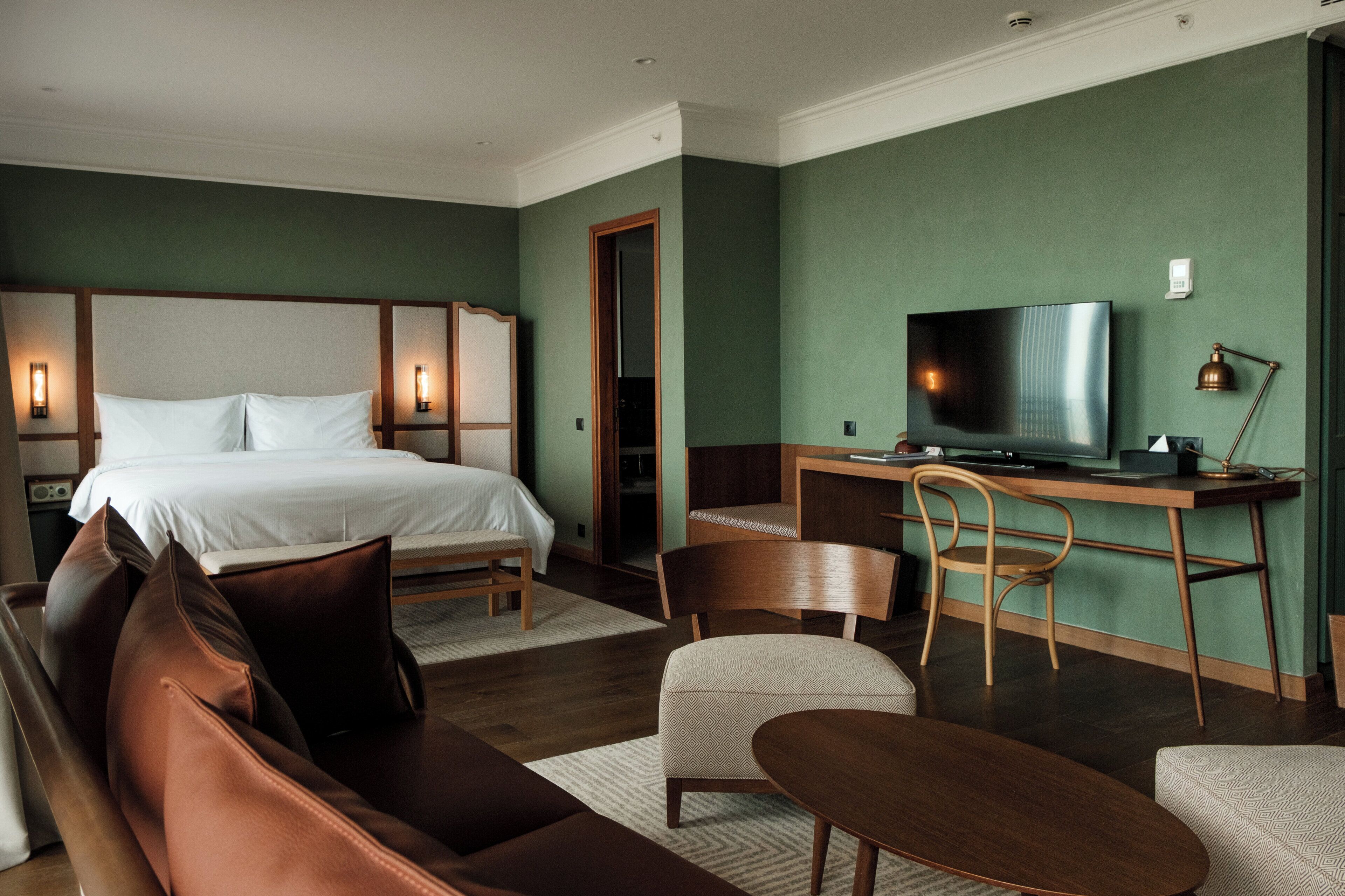 A hotel room with a bed, a desk with a television, a chair, and a sofa.