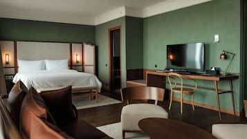 A hotel room with a bed, a desk with a television, a chair, and a sofa.
