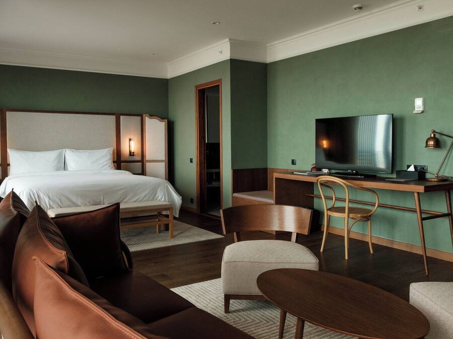 A hotel room with a bed, a desk with a television, a chair, and a sofa.